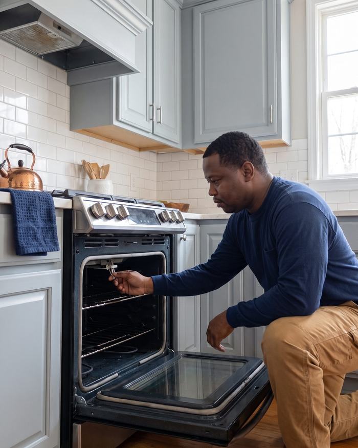 Technician checking the inside of an open oven door in a kitchen